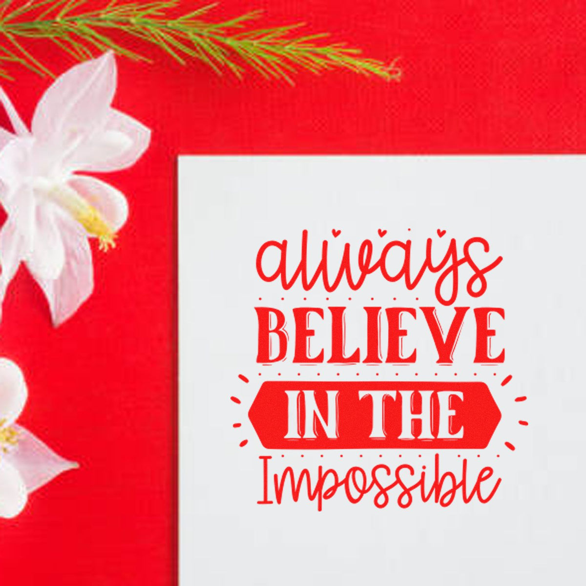 Red stamp seal product with Always believe in the impossible on white, against a bright red background with white flowers.