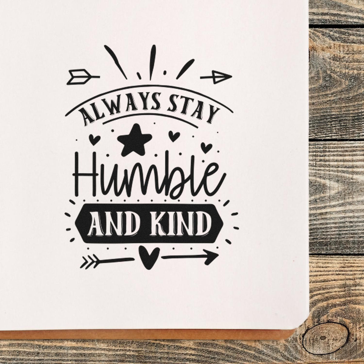 Black decorative stamp seal reading Always Stay Humble and Kind with arrows, hearts, and star on white background.