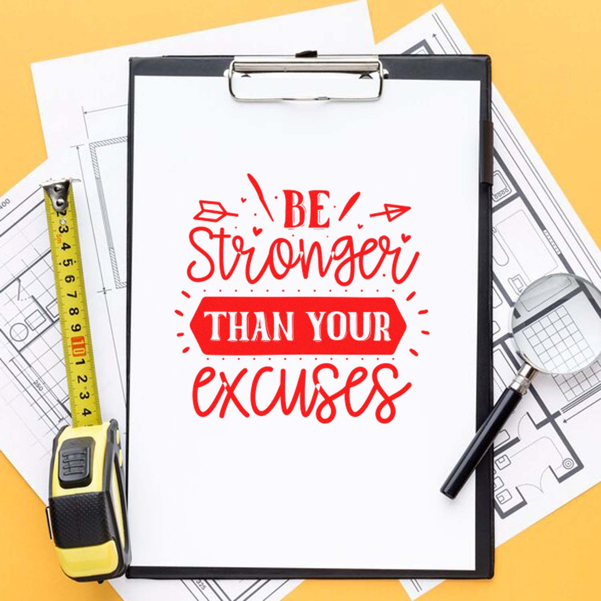 Clipboard with red stamp-and-seal reading Be stronger than your excuses, plus tape measure, blueprints and magnifier.