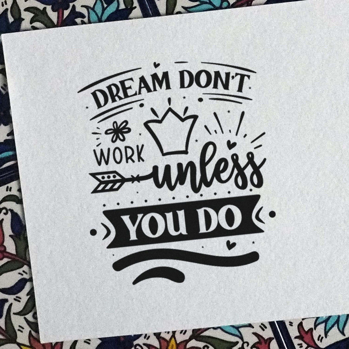 Black stamp seal design on white paper reading Dream dont work unless you do, with crown, arrow, and heart accents.