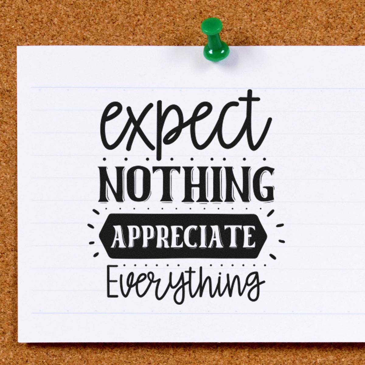 Green push pin holds a white card on corkboard with black decorative stamp text: expect nothing, appreciate everything.
