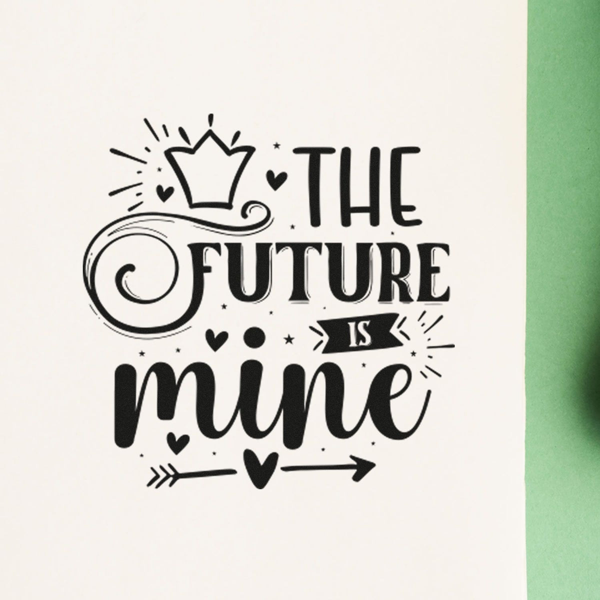 Black decorative rubber stamp reading The Future Is Mine with crown, hearts and arrows on white paper, green edge.