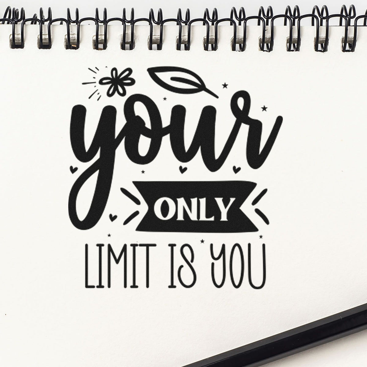 Black-and-white stamp-style design on spiral notebook reading your only limit is you, with leaf and floral accents.