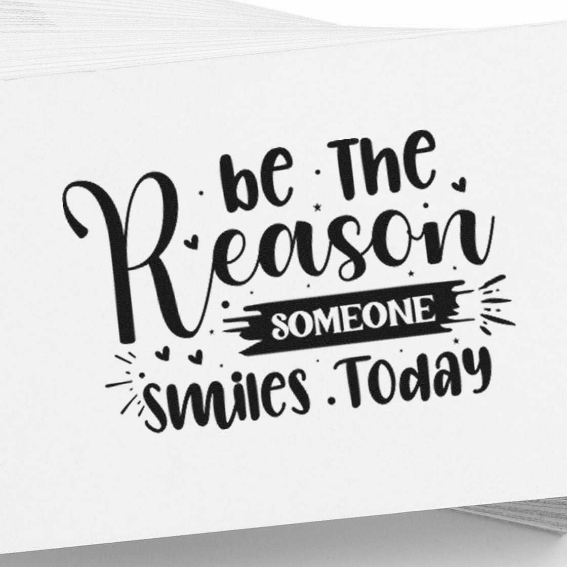 Black rubber stamp with hand-lettered quote Be the reason someone smiles today on white paper.