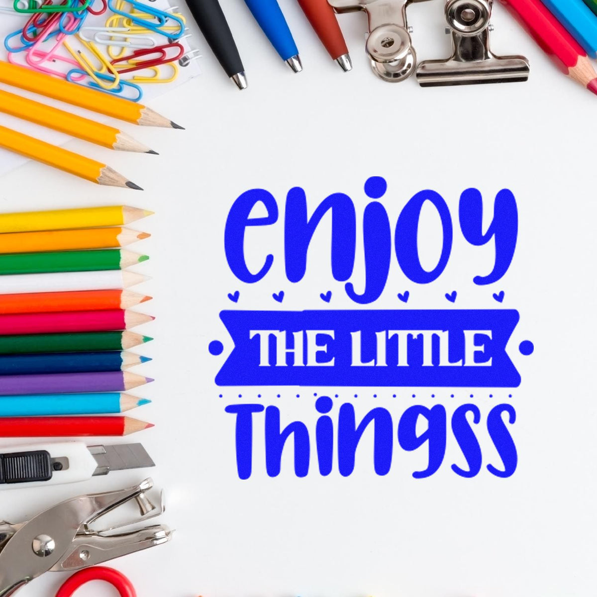 Blue stamp-and-seal design reading enjoy the little things, framed by colorful pencils, clips, pens, and office tools.