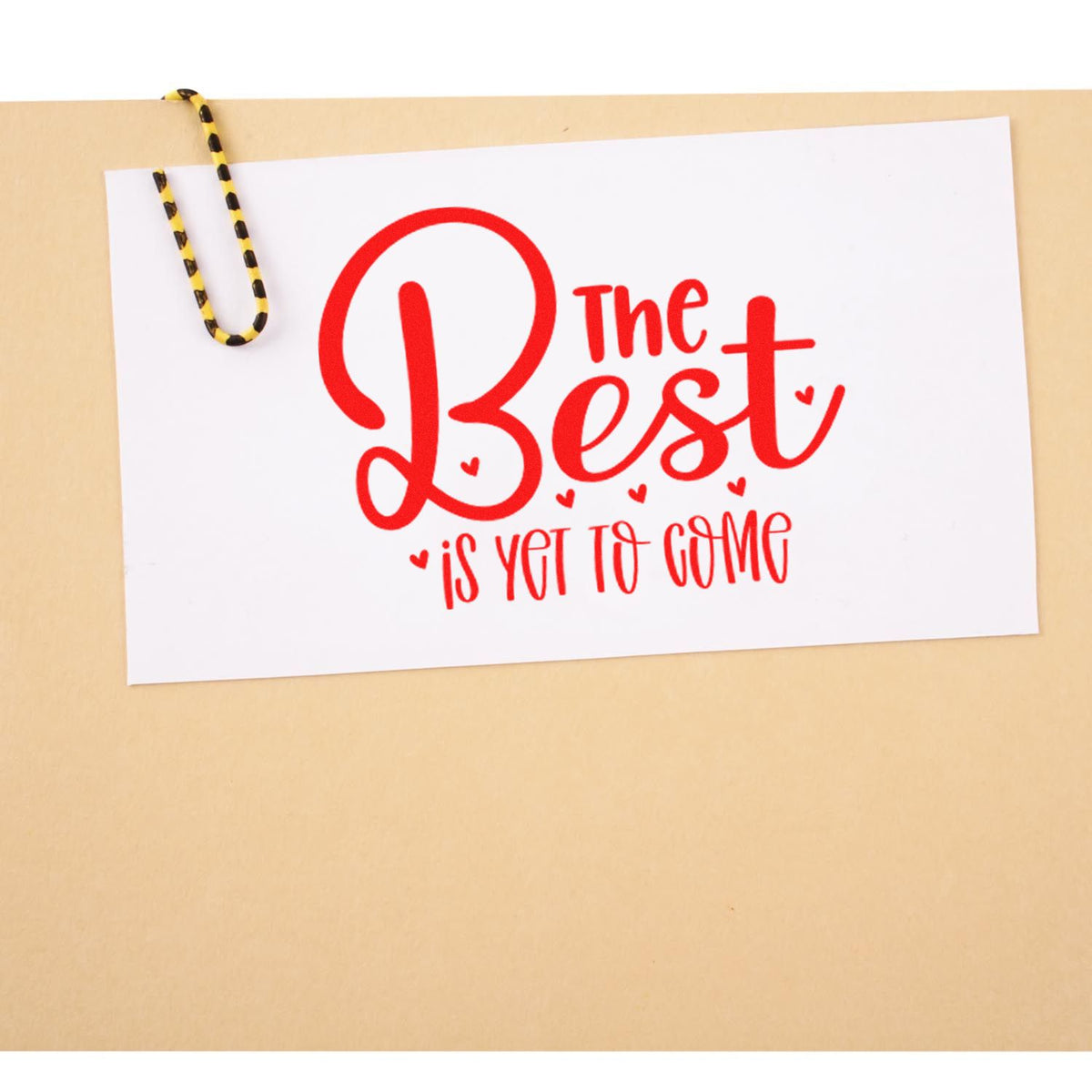 White card with red script The Best is Yet to Come, clipped with a black-and-yellow paper clip, custom stamp and seal design.