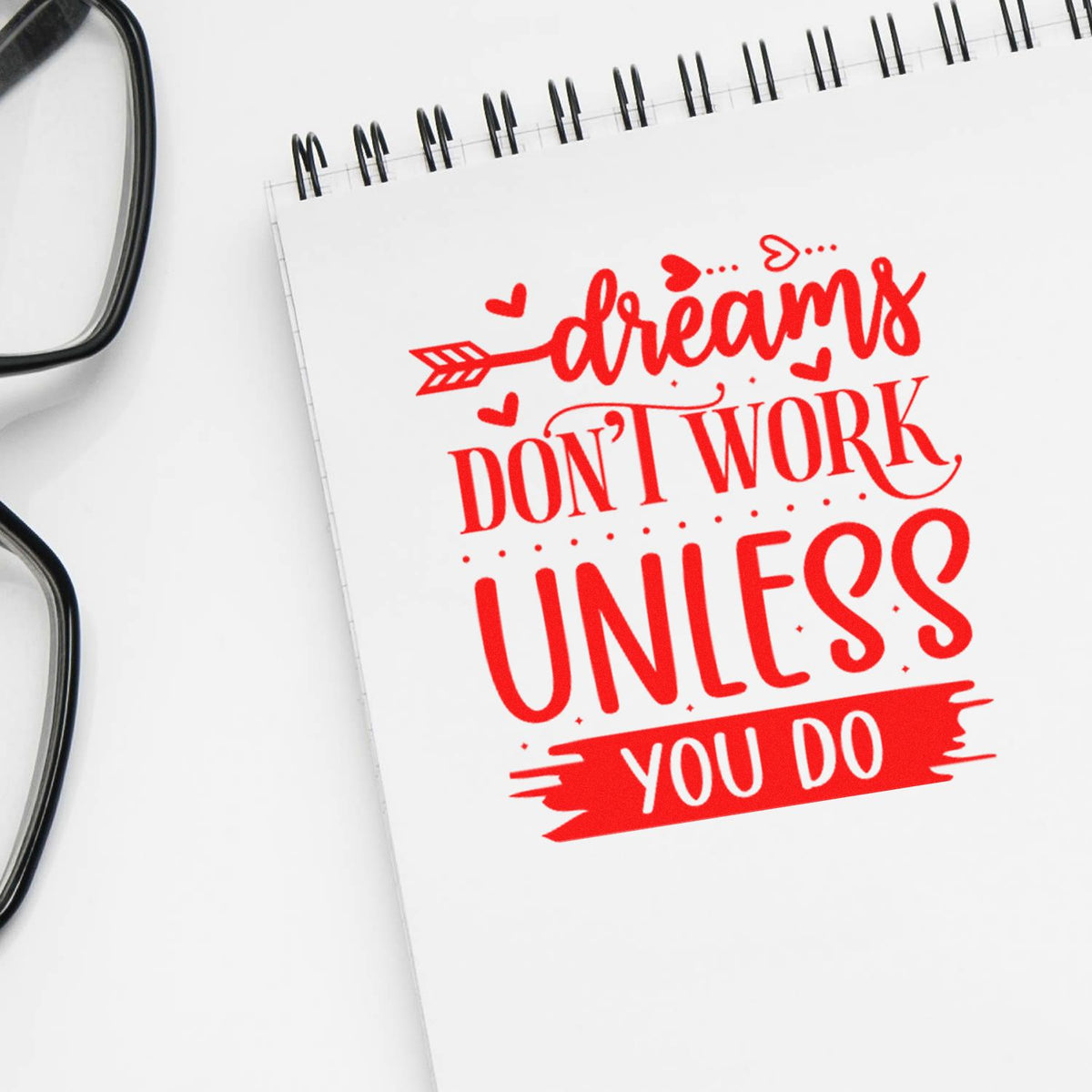 Red stamp-style seal on white spiral notebook with hearts: Dreams dont work unless you do.