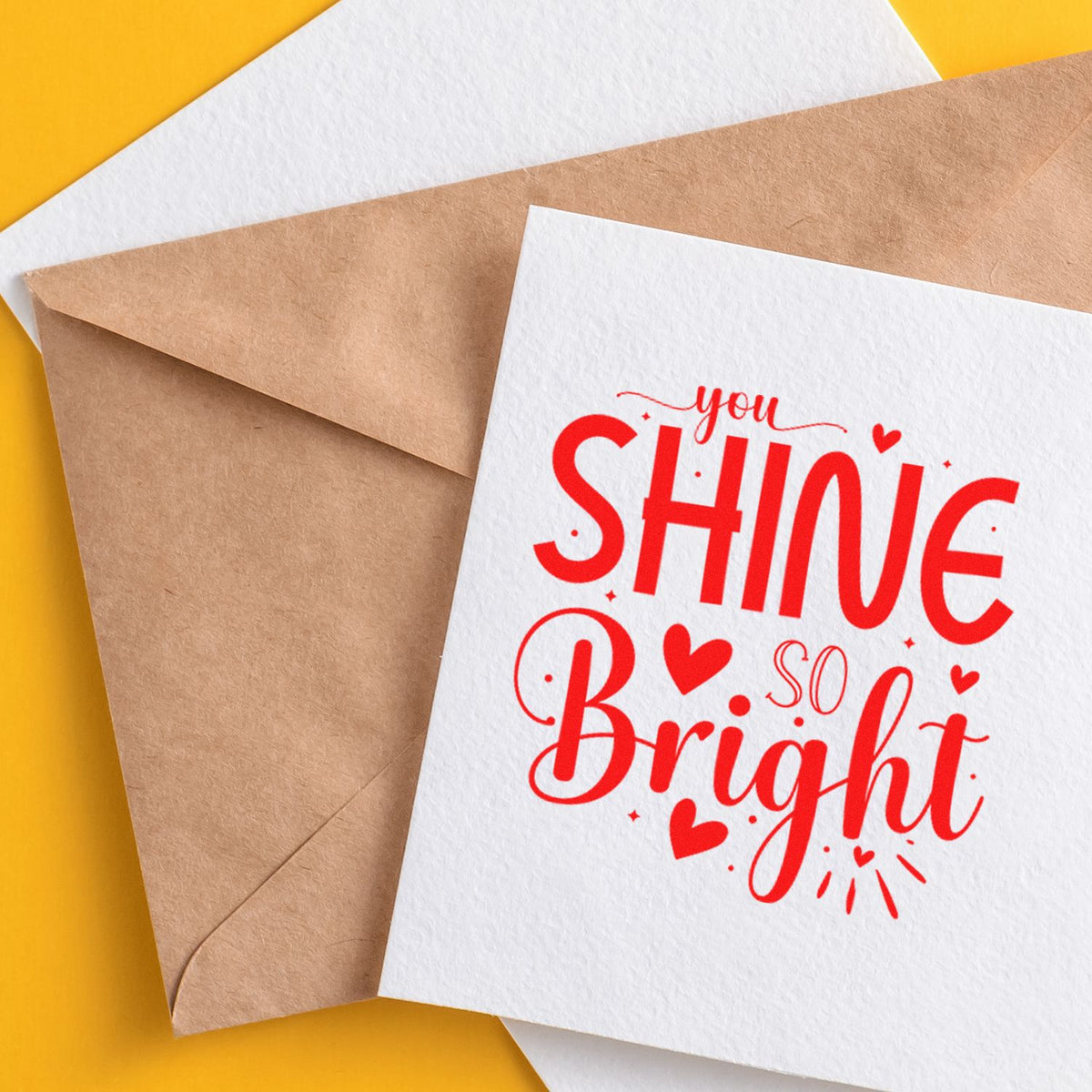 Red You shine so bright stamp design on white card, beside a kraft envelope and white sheet on a yellow background.
