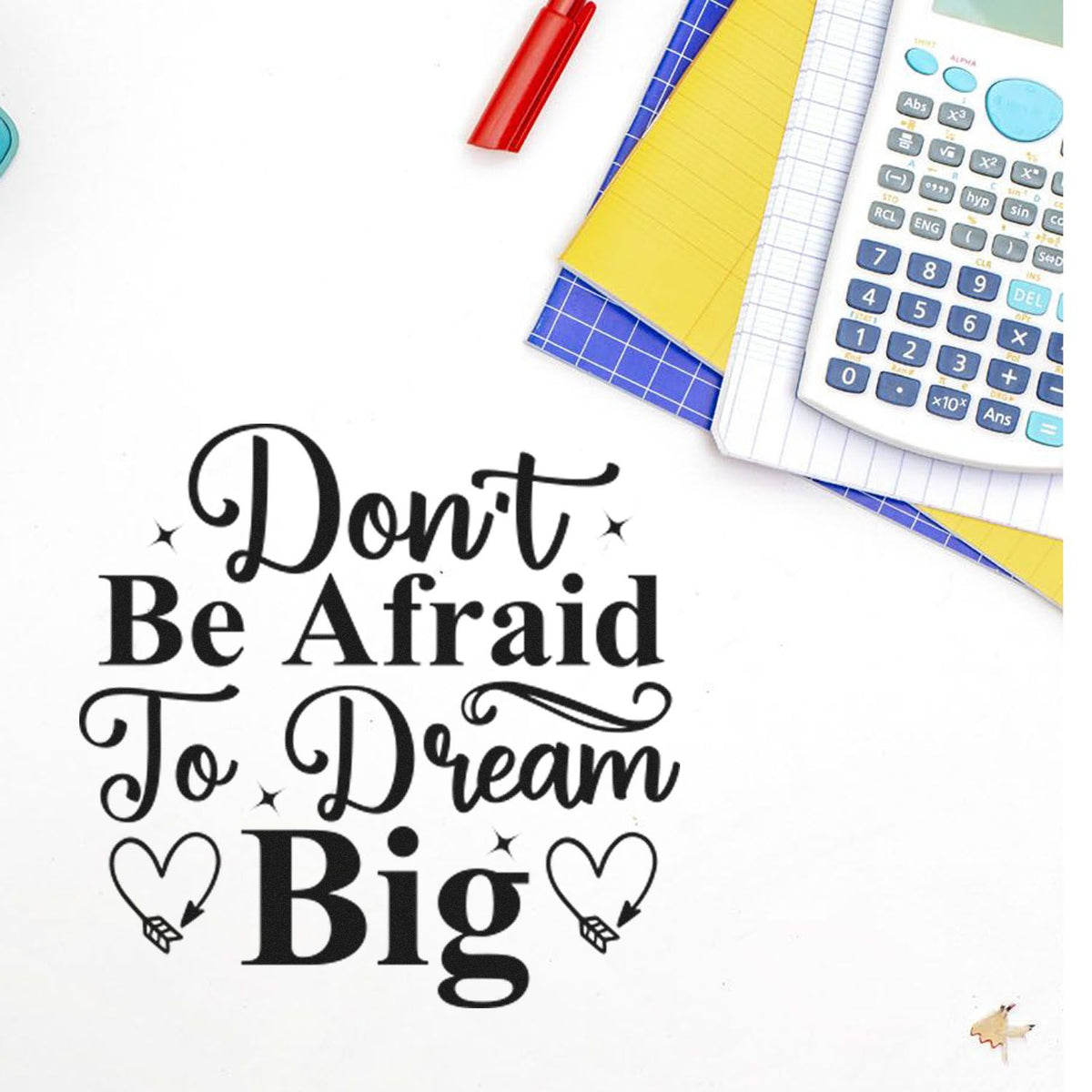Black decorative stamp seal with Dont Be Afraid To Dream Big, on white background with calculator, notebooks, and red pen.