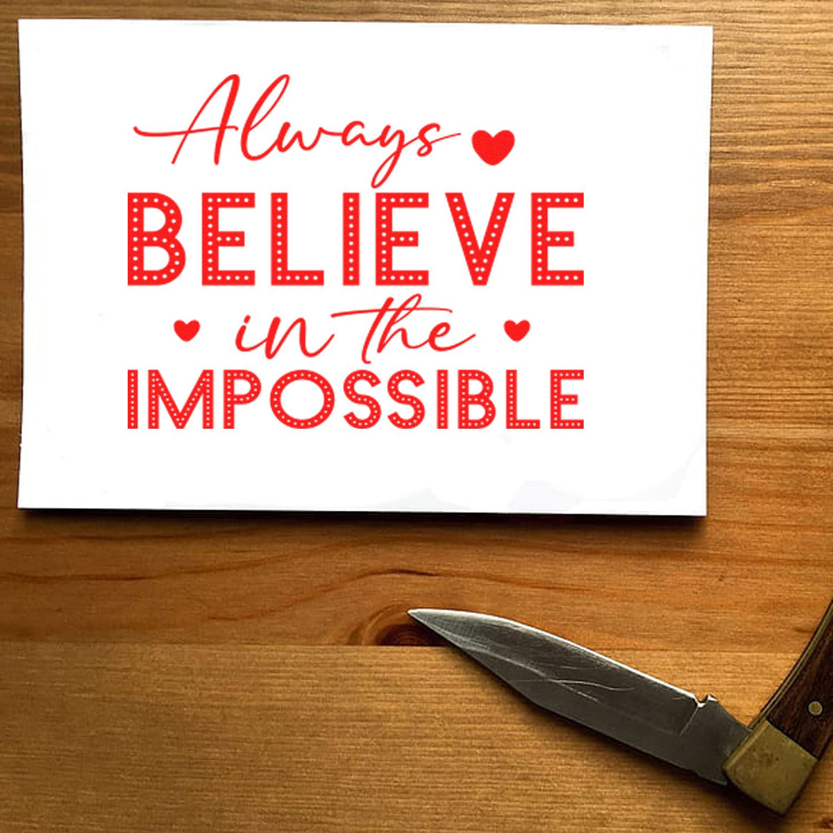 Red stamp and seal design reading Always believe in the impossible on white paper with heart accents.