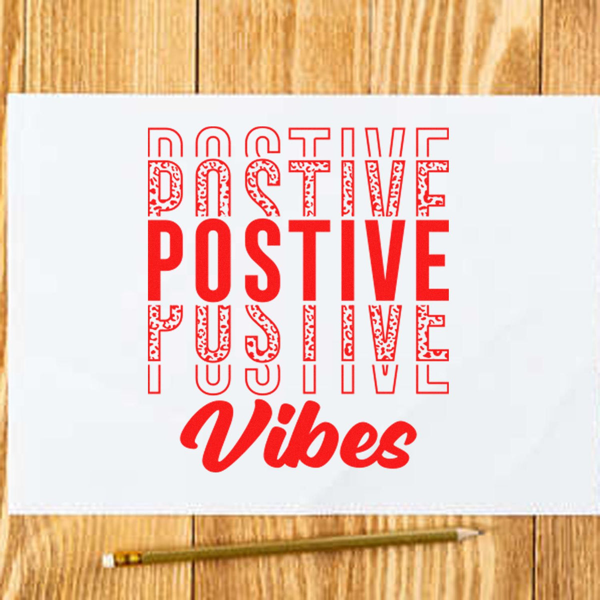 Red Positive Vibes stamp and seal design on white paper, layered typography, with a pencil on a wood tabletop.