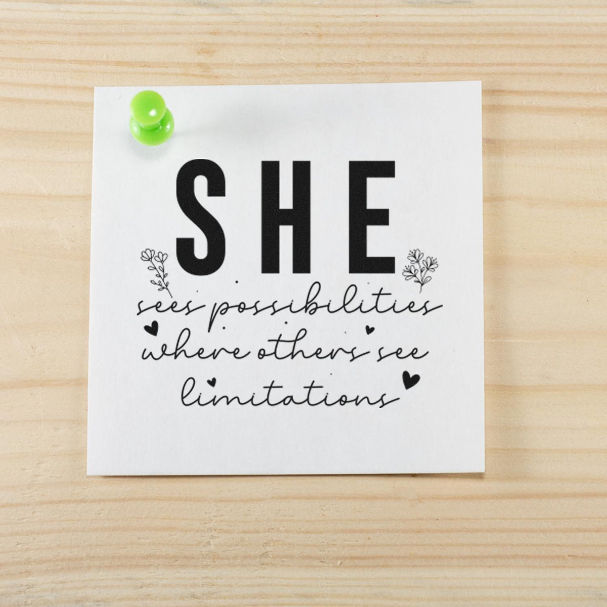 Custom stamp seal on white card with black SHE sees possibilities quote, green pushpin, on light wood background.