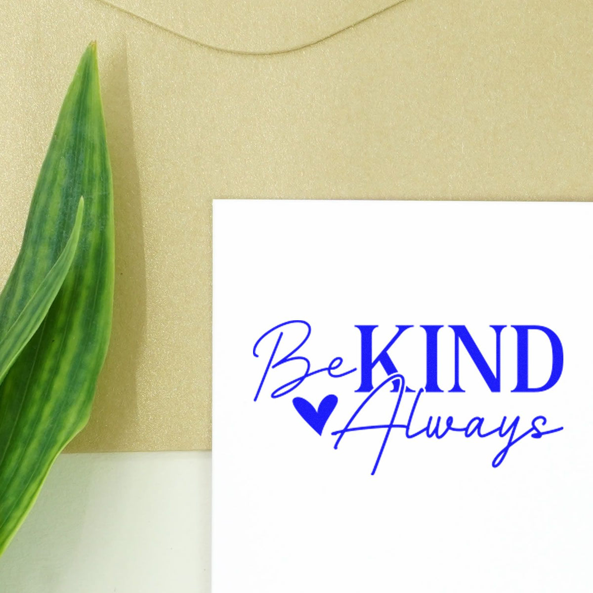 Blue Be KIND Always stamp and seal on white card with heart, beside a green leaf on a beige background