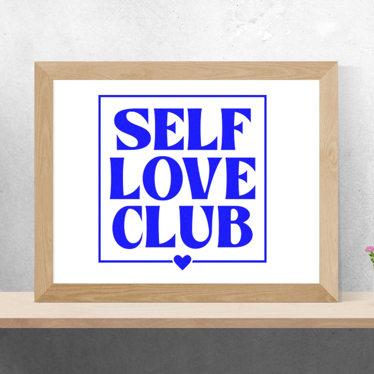 Blue SELF LOVE CLUB stamp-style seal with heart in a light wood frame on a white background.