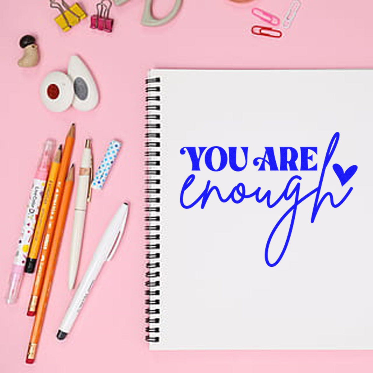 Pink flat lay with stamp and seal tools, pens, and a spiral notebook reading YOU ARE enough in blue.