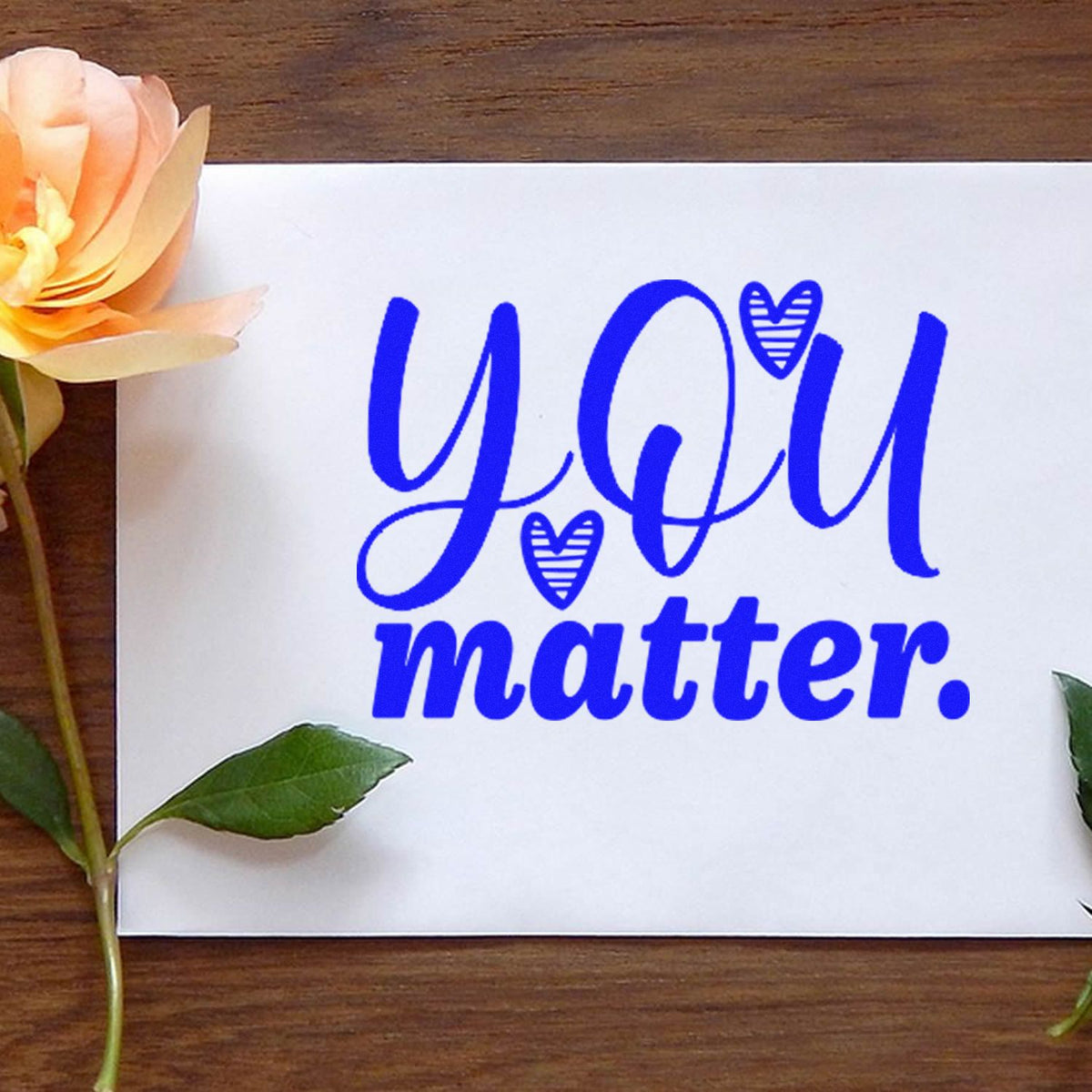 Blue custom rubber stamp and seal reading YOU matter. with heart icons on a white card, accented by flowers.