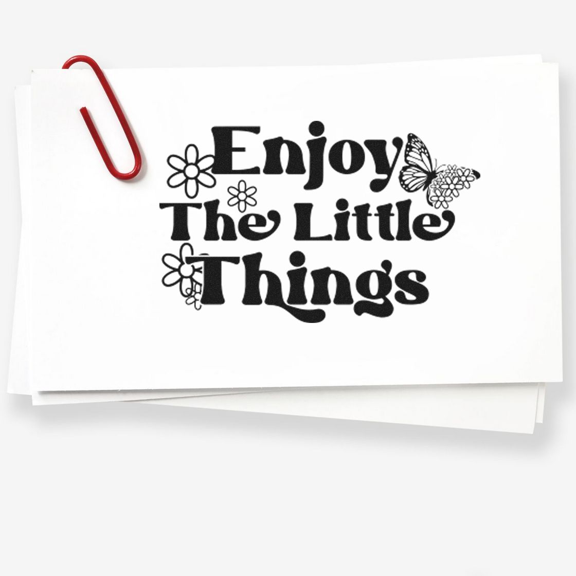Black decorative stamp and seal on white cards with red paperclip, reading Enjoy The Little Things with flowers and butterfly.