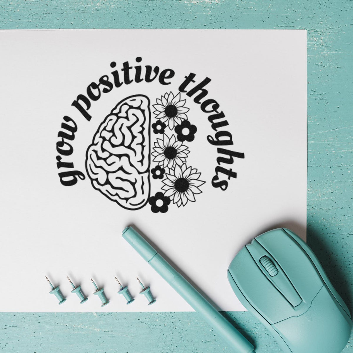 Teal stamp and seal tools beside a white sheet with a black grow positive thoughts brain-and-flowers stamp.