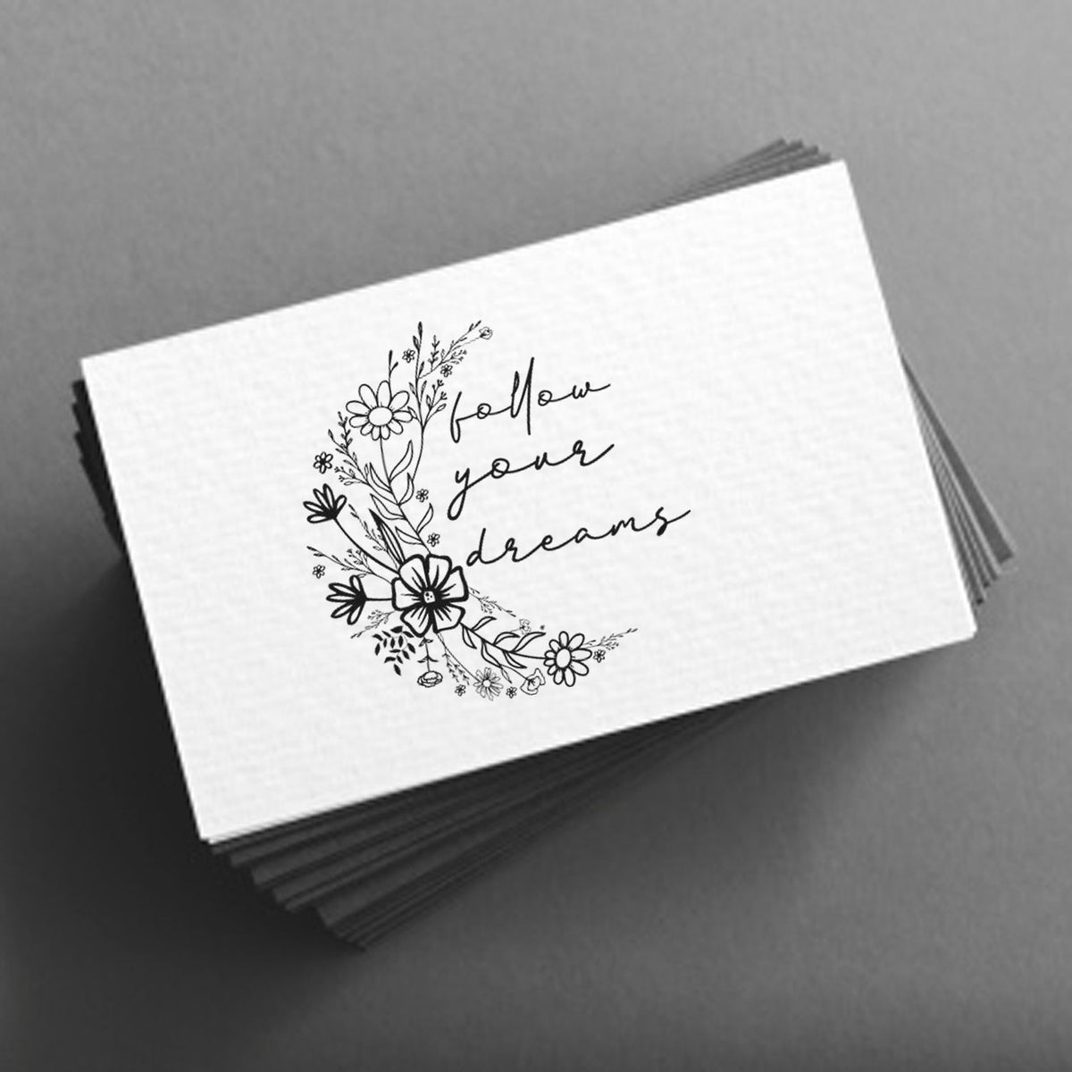 Stack of white stamp and seal cards with black floral wreath and follow your dreams script on gray background.