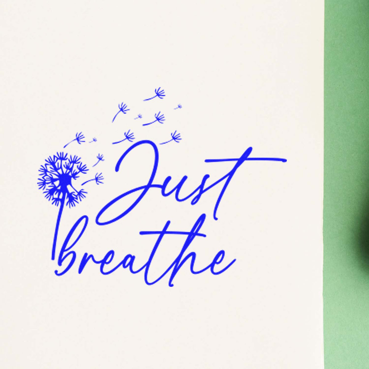 Blue Just Breathe dandelion stamp and seal design on white paper with a green edge.