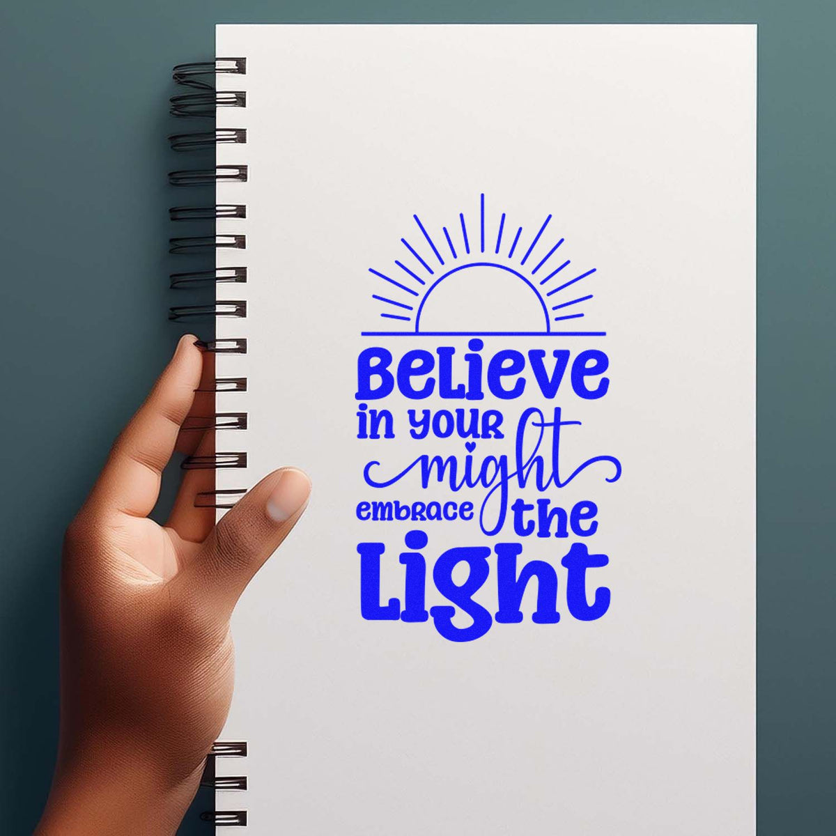 Blue stamp design on white spiral notebook: Believe in your might, embrace the light with sunrise icon.