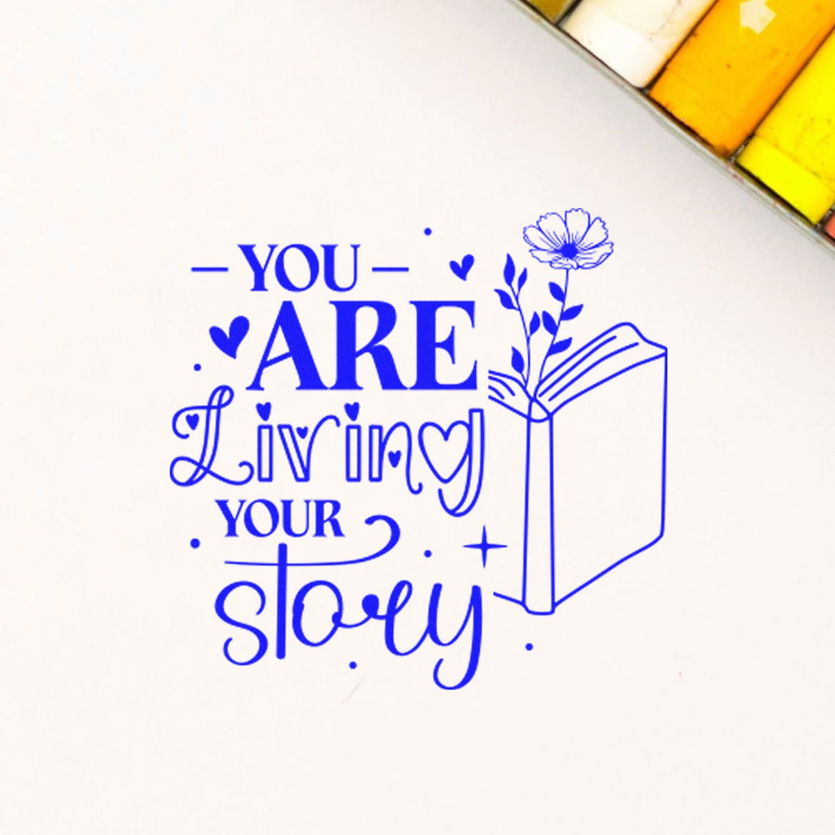 Blue rubber stamp and seal design reading You are living your story with hearts, flower and open book on white.