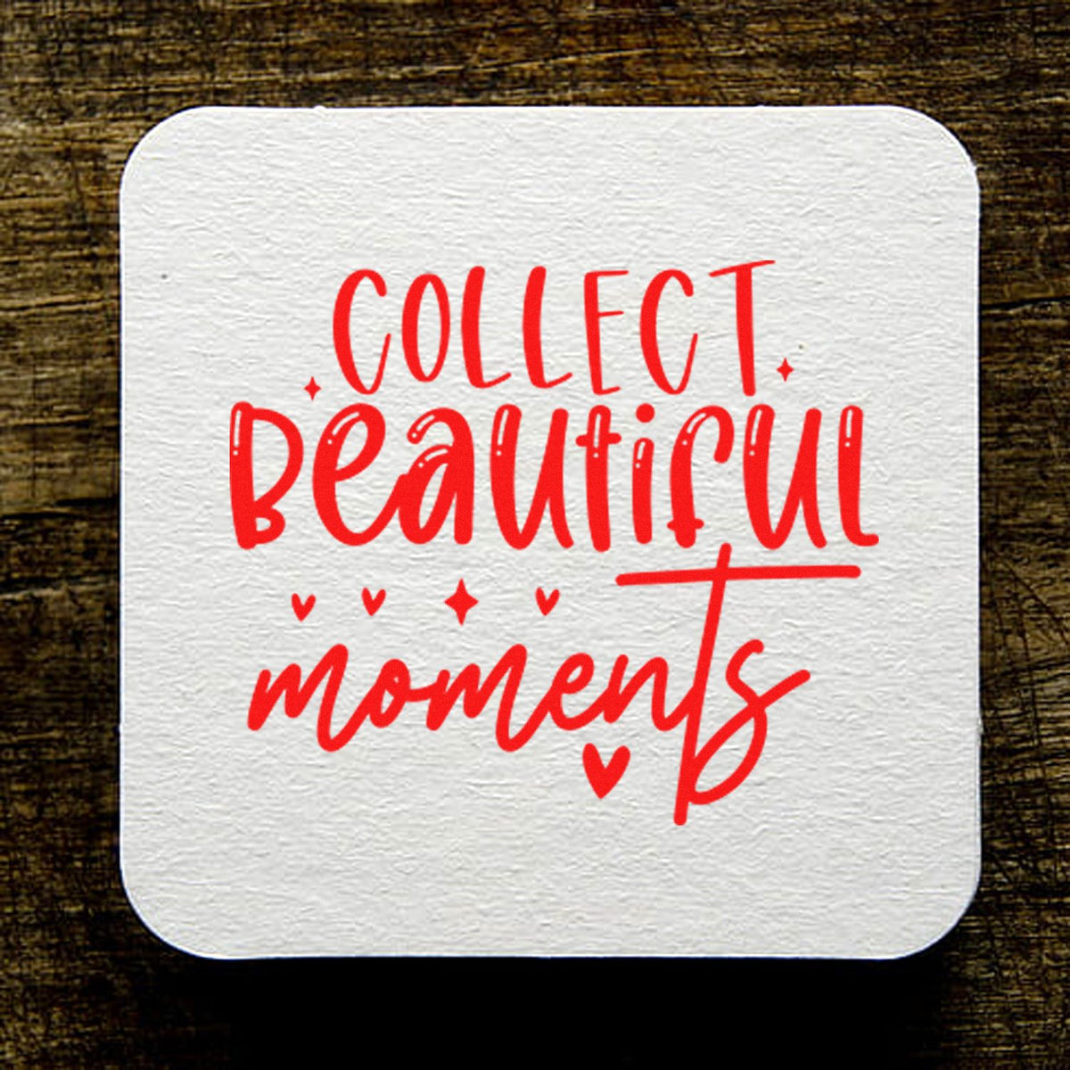 White textured square stamp seal with red Collect beautiful moments lettering and hearts on a dark wood background.