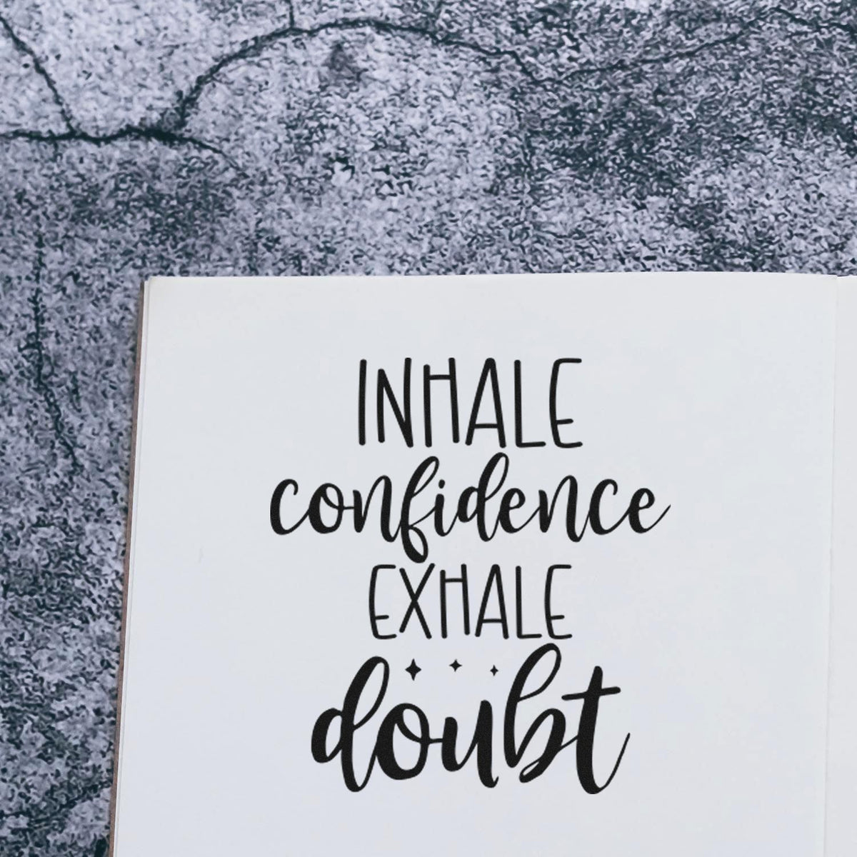 Black stamp-style seal reading Inhale confidence, exhale doubt on a white card with a gray textured background.