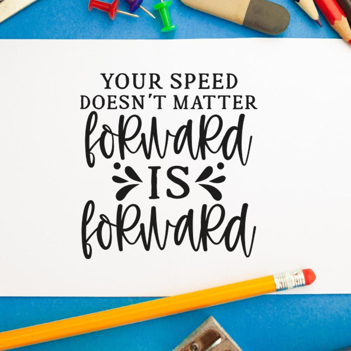 Black custom stamp/seal design on white paper: Your speed doesnt matter, forward is forward, with blue background and pencils.