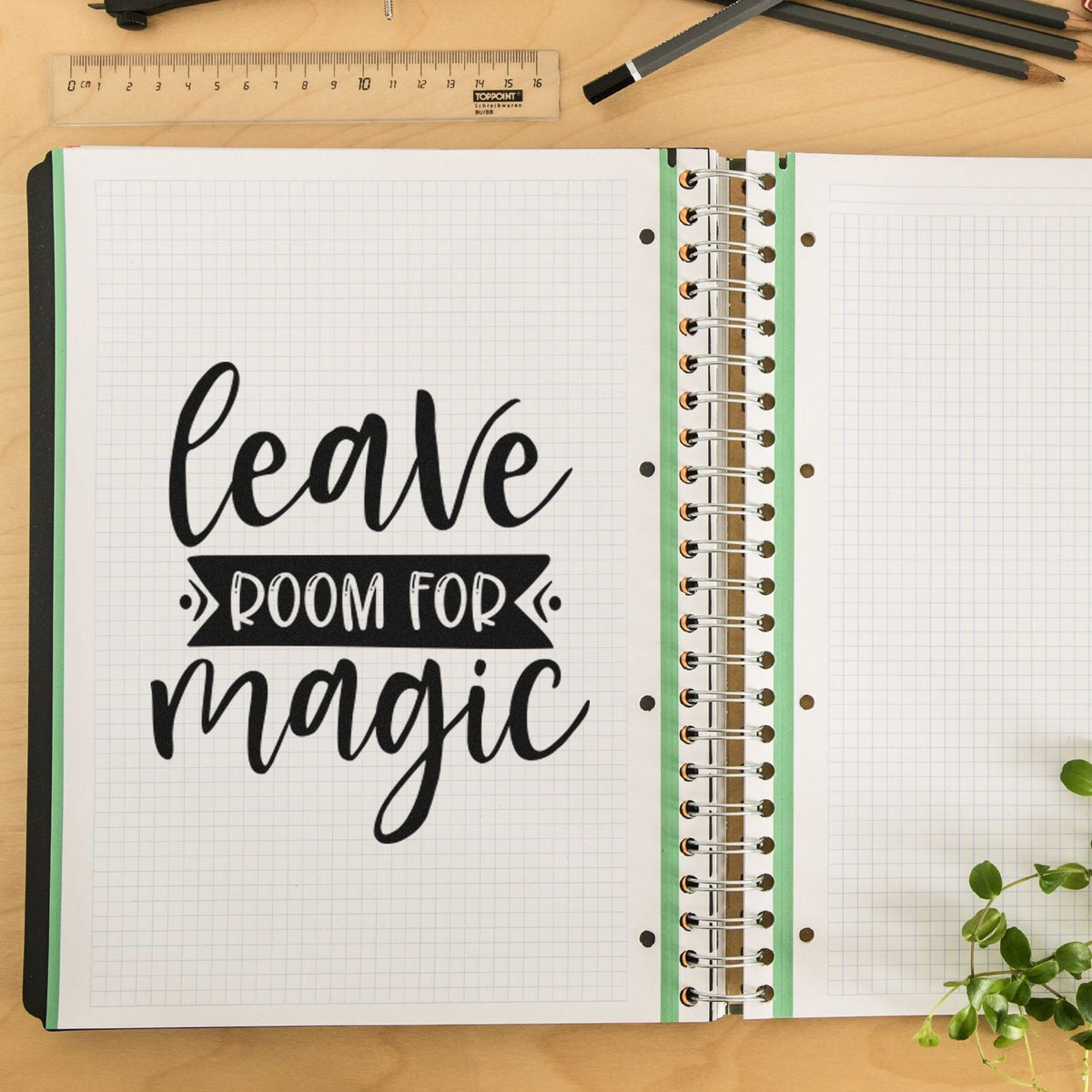 Black rubber stamp and seal reading leave room for magic on a white grid notebook with green binding and spiral rings.