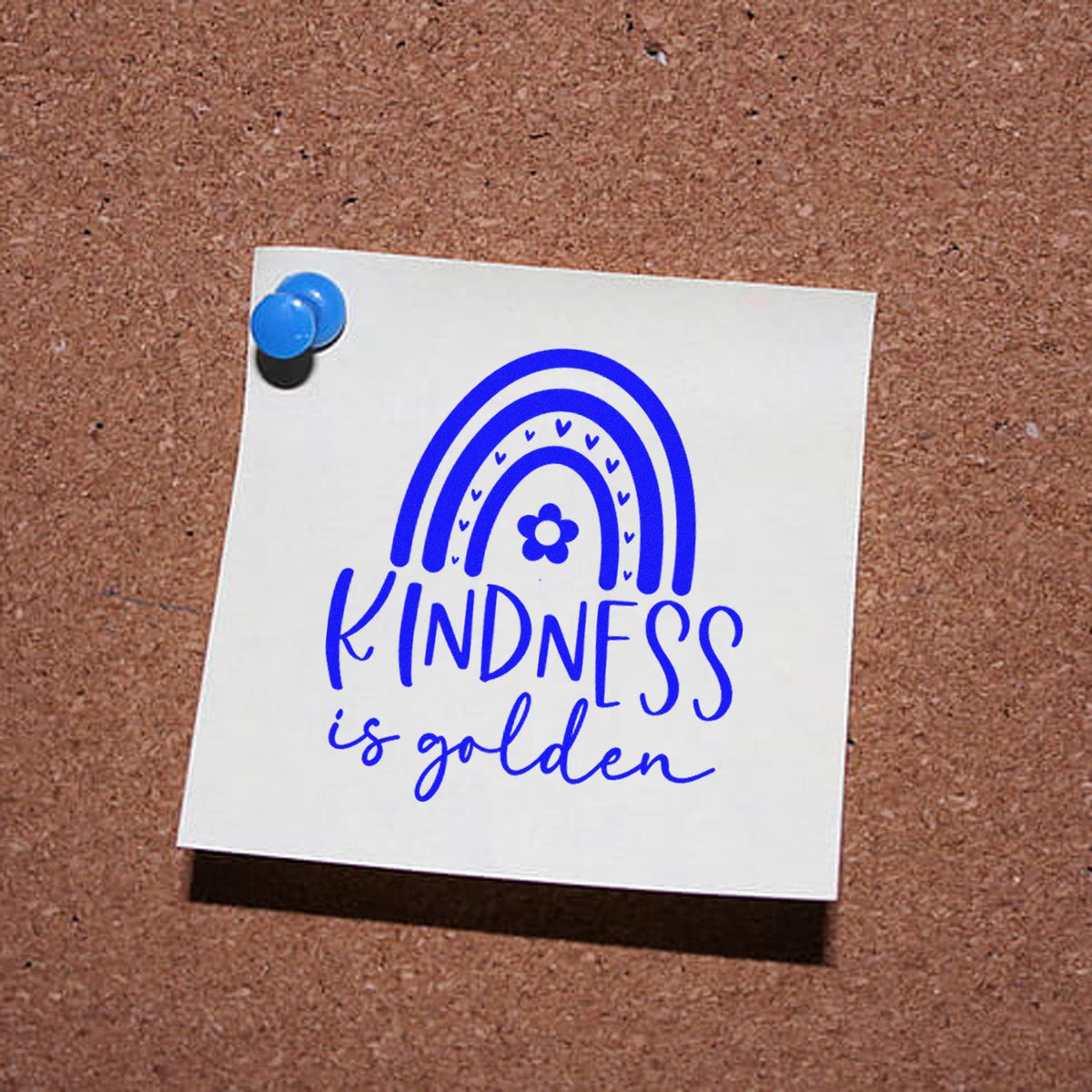 Blue kindness stamp and seal design on white note pinned to corkboard, with rainbow, flower, and kindness is golden text.