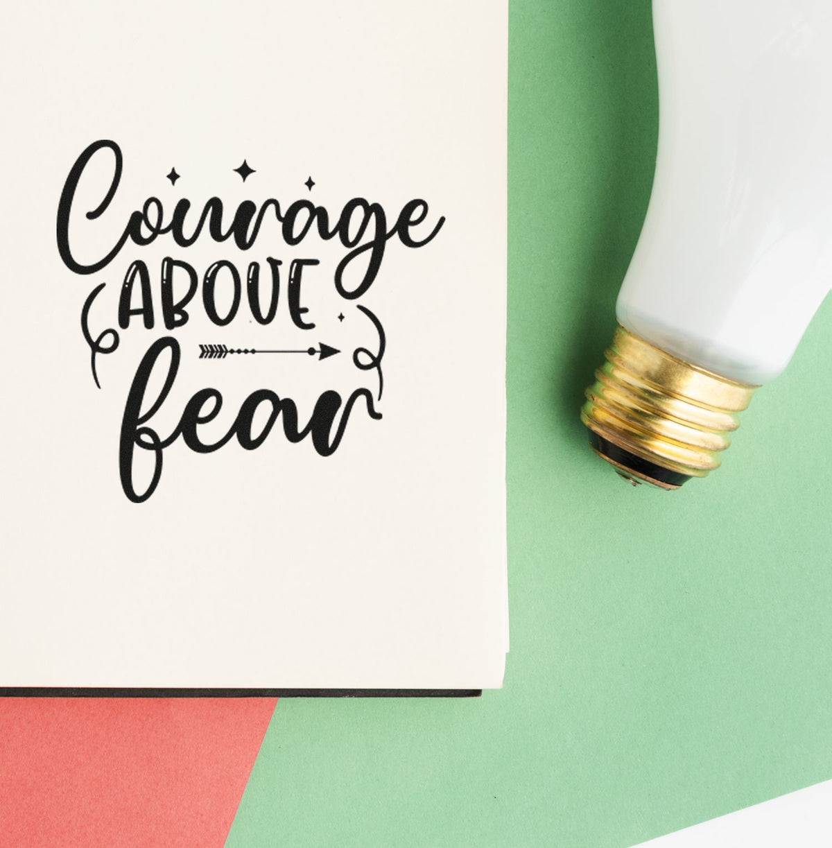 Black Courage Above Fear stamp design on white paper, beside a white-and-gold seal tool on green and coral background.