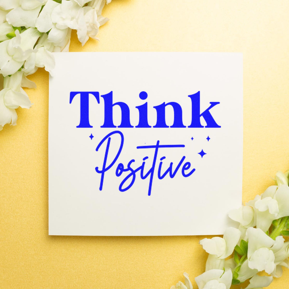 Blue Think Positive stamp and seal on a white card, framed by white flowers on a soft yellow background.