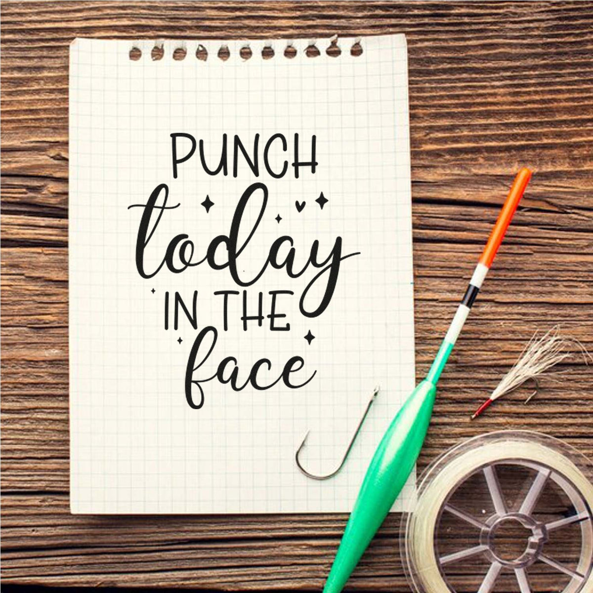 Rubber stamp reading Punch today in the face on grid paper, with green sealing tool, orange brush, and clear tape on wood.