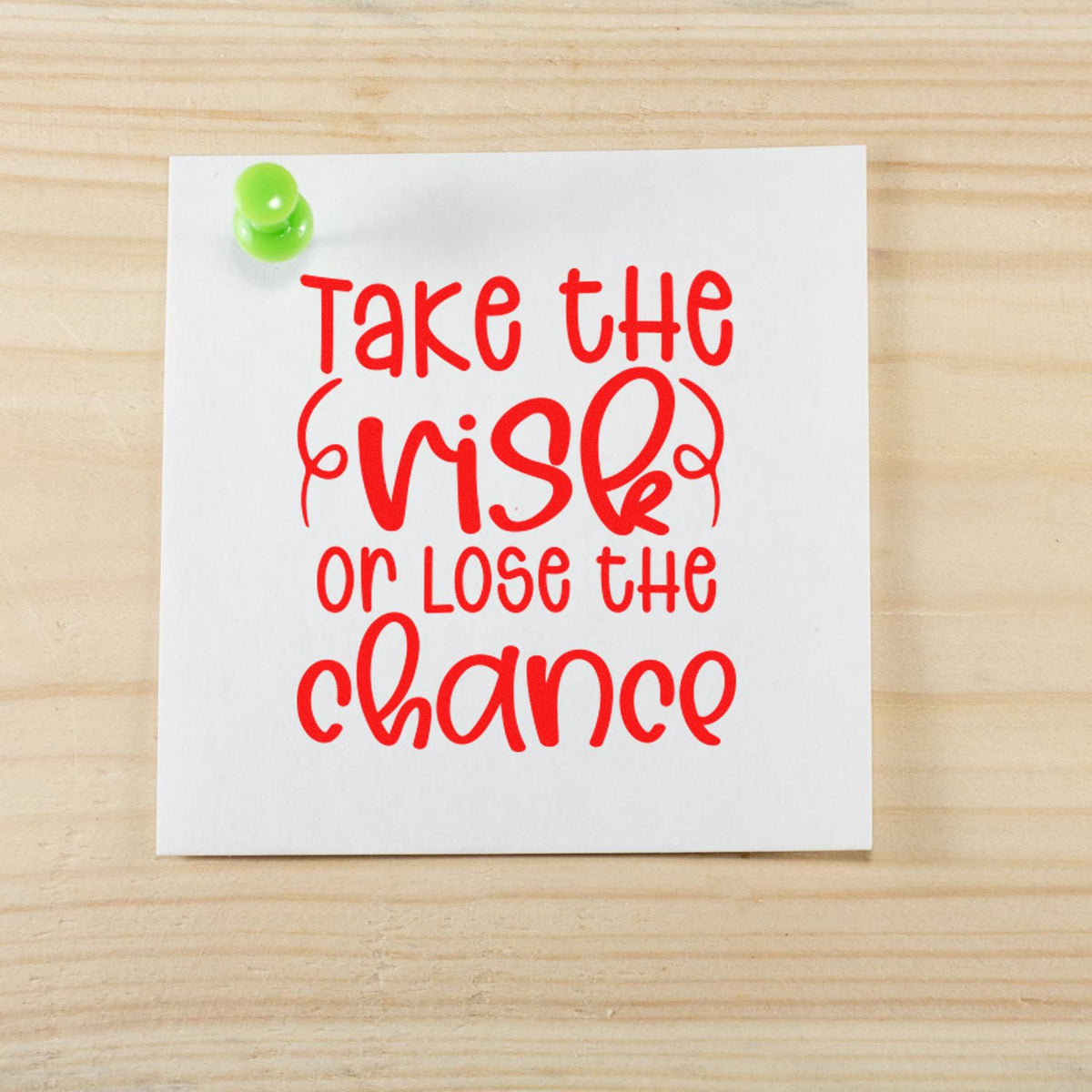 Custom rubber stamp and seal with red Take the risk or lose the chance text on white paper, pinned with a green pushpin.