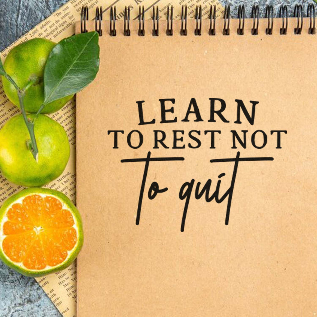 Custom stamp design on a brown notebook, reading Learn to rest not to quit, with green leaves and orange citrus slices.