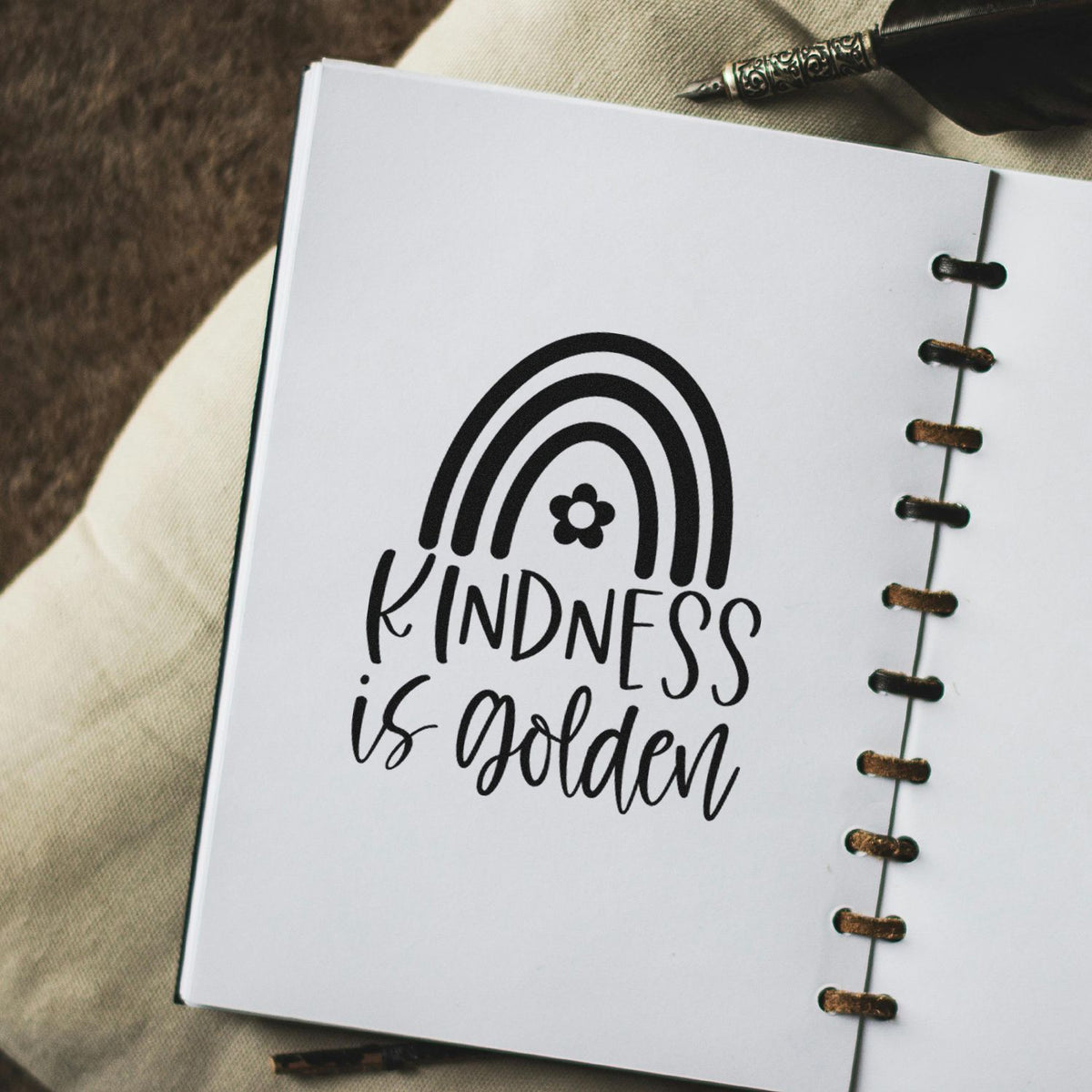 Black kindness is golden stamp/seal design on white notebook page with rainbow graphic and copper spiral binding.