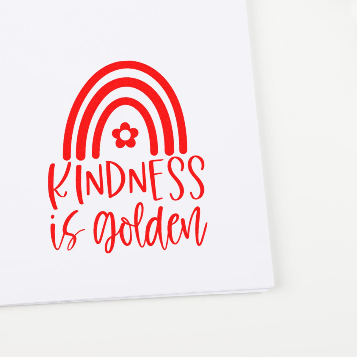 Red stamp-style rainbow and flower seal reading Kindness is golden on white paper.