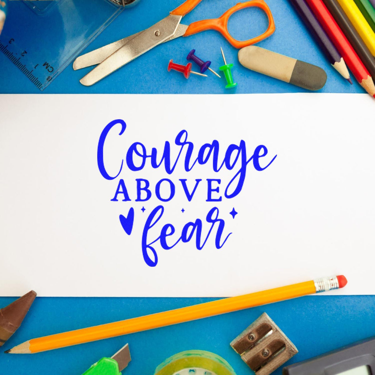 Blue Courage above fear stamp design on white card, framed by colorful school supplies on blue background.
