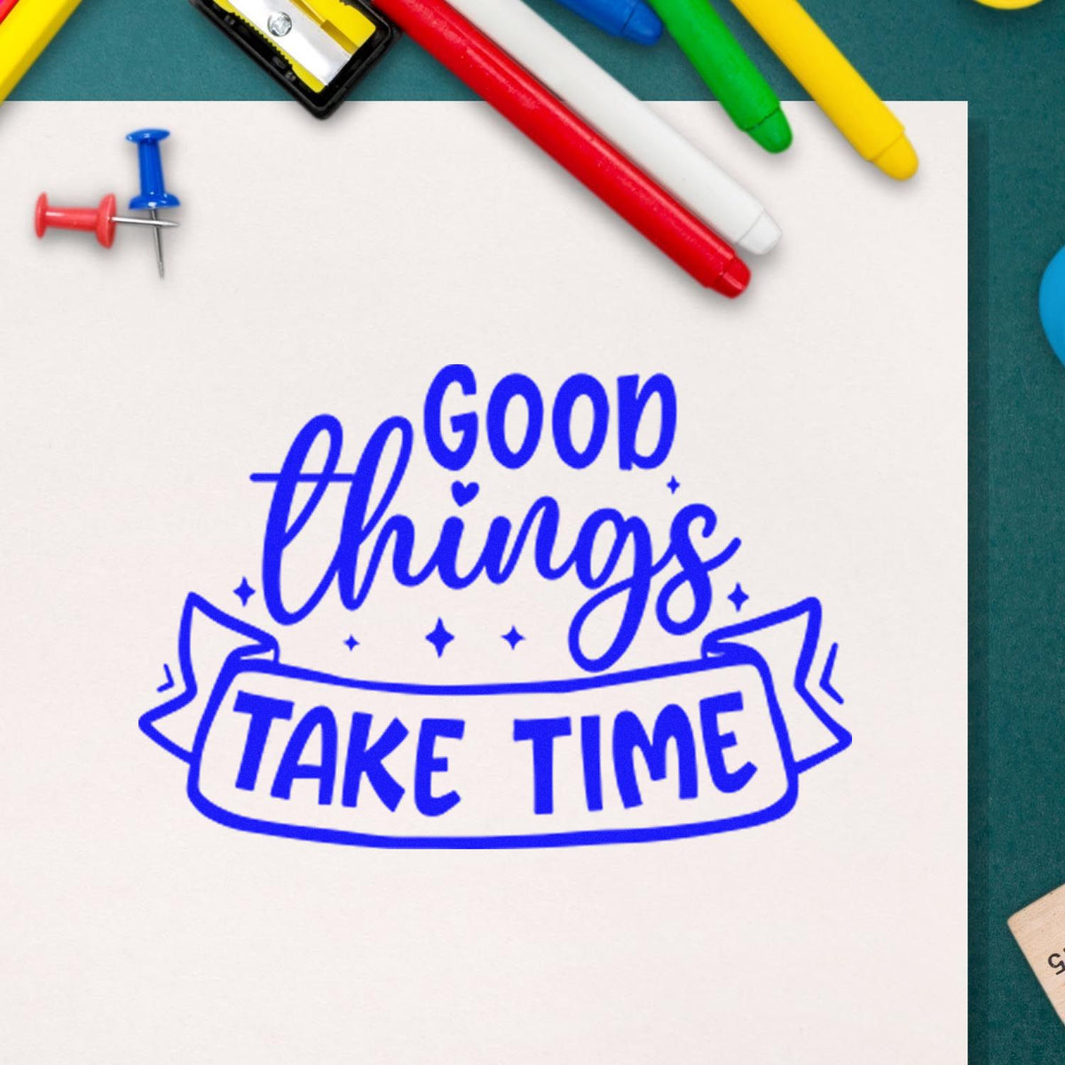 Blue stamp seal with Good Things Take Time on white paper, surrounded by colorful pens and push pins.