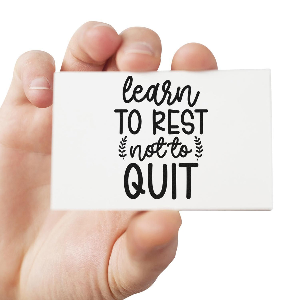 White rubber stamp with black learn to rest not to quit text held in a hand, a motivational seal product.
