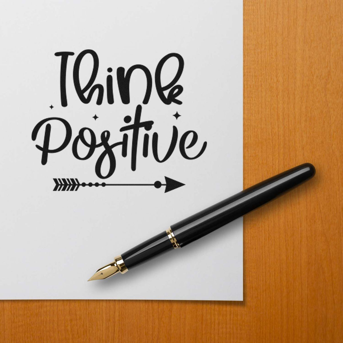 Custom black stamp and seal reading Think Positive on white paper, with a black-and-gold fountain pen on a wood desk.
