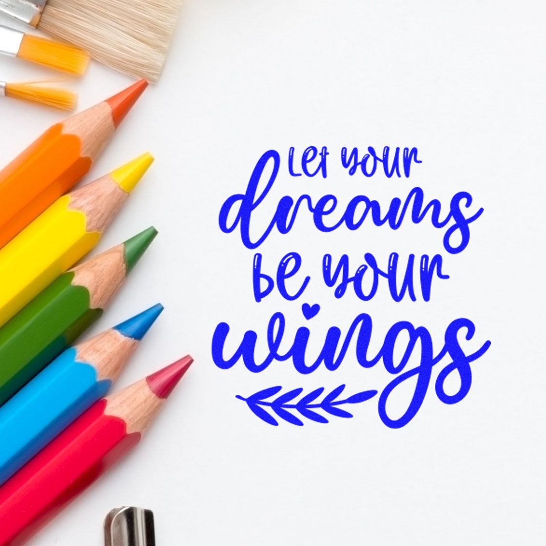 Blue stamp and seal design reading let your dreams be your wings with colorful pencils on white paper.