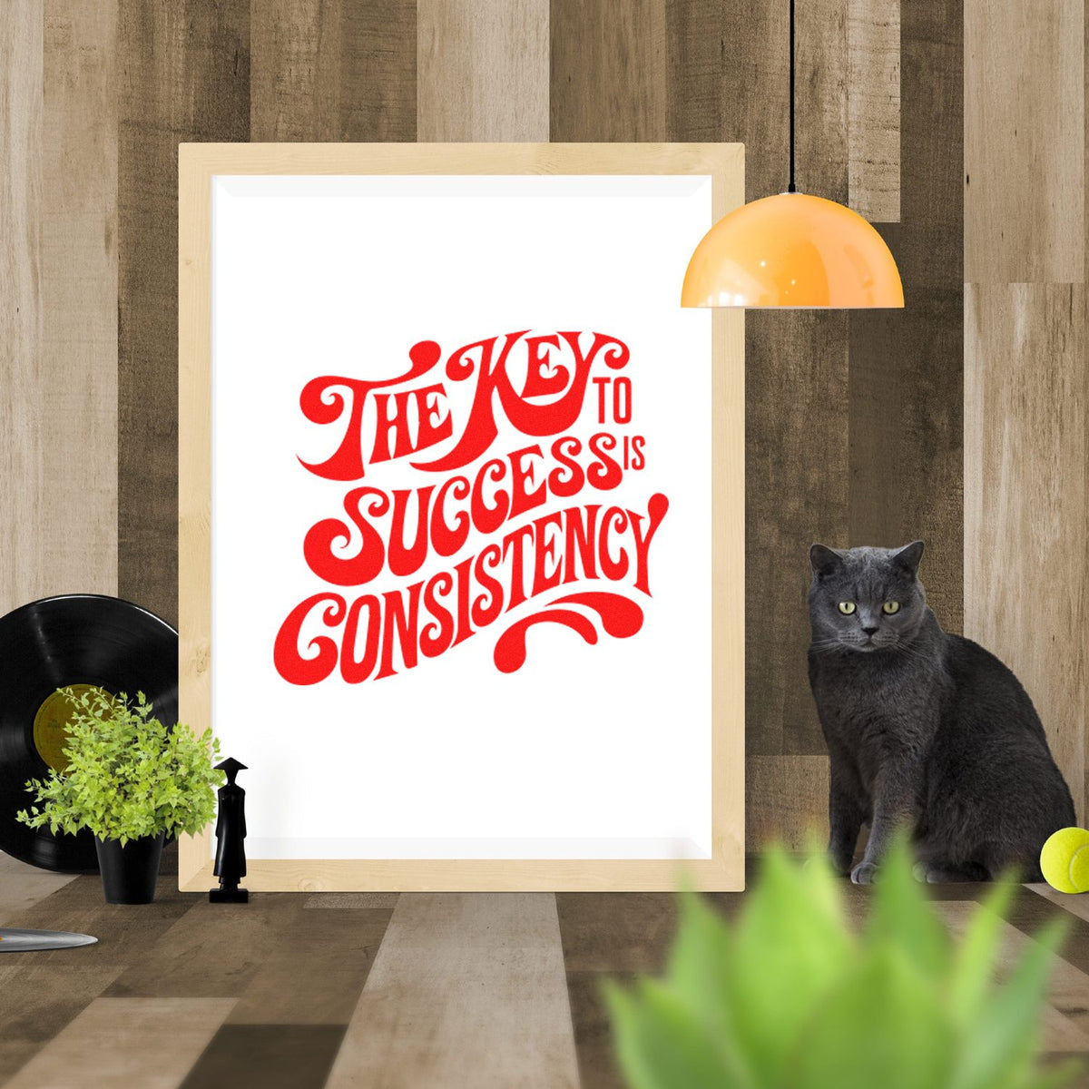 Framed stamp-and-seal design with bold red The key to success is consistency lettering on white, against a wood backdrop.