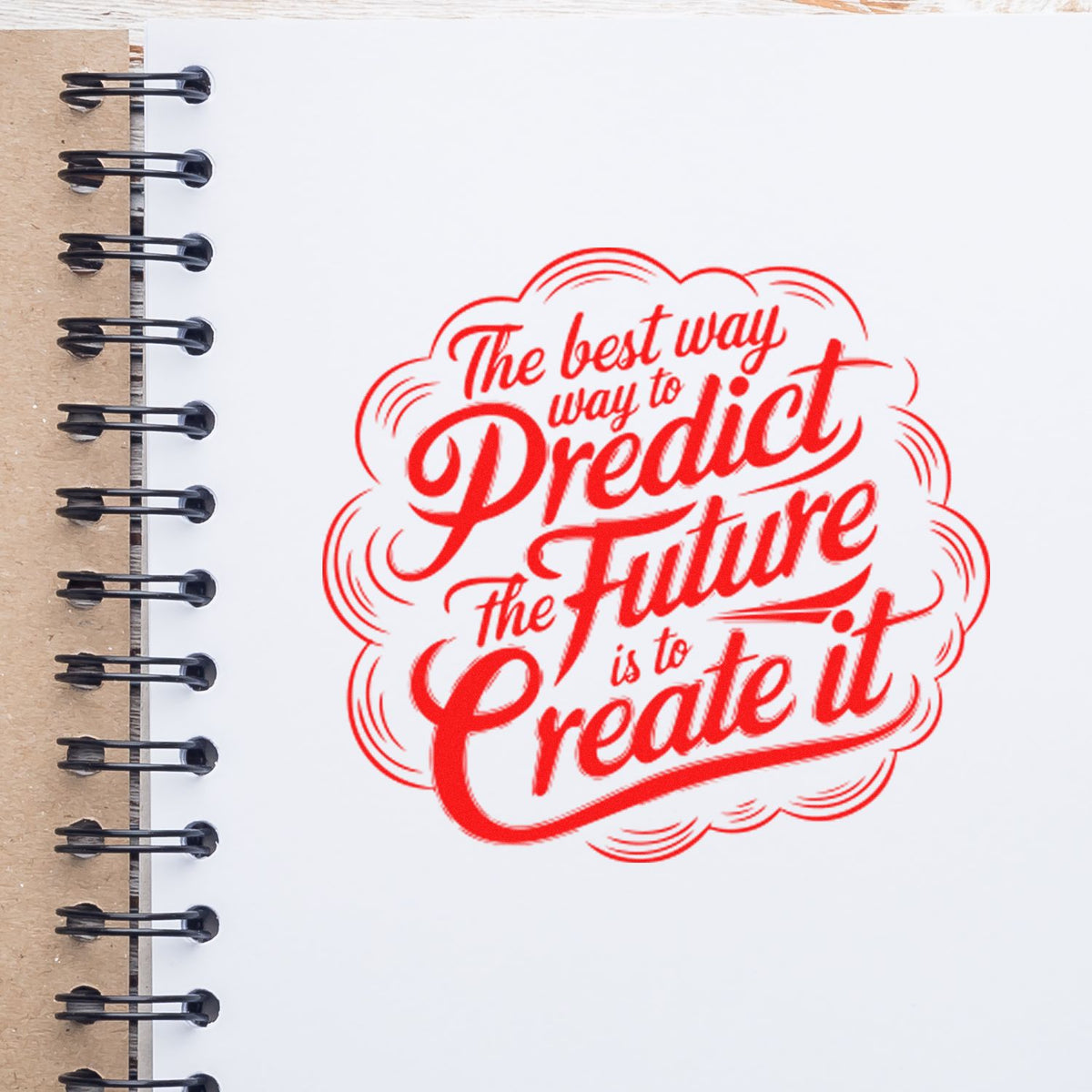 Red motivational rubber stamp seal reading Predict Future Create It on a white notebook page with black spiral binding.