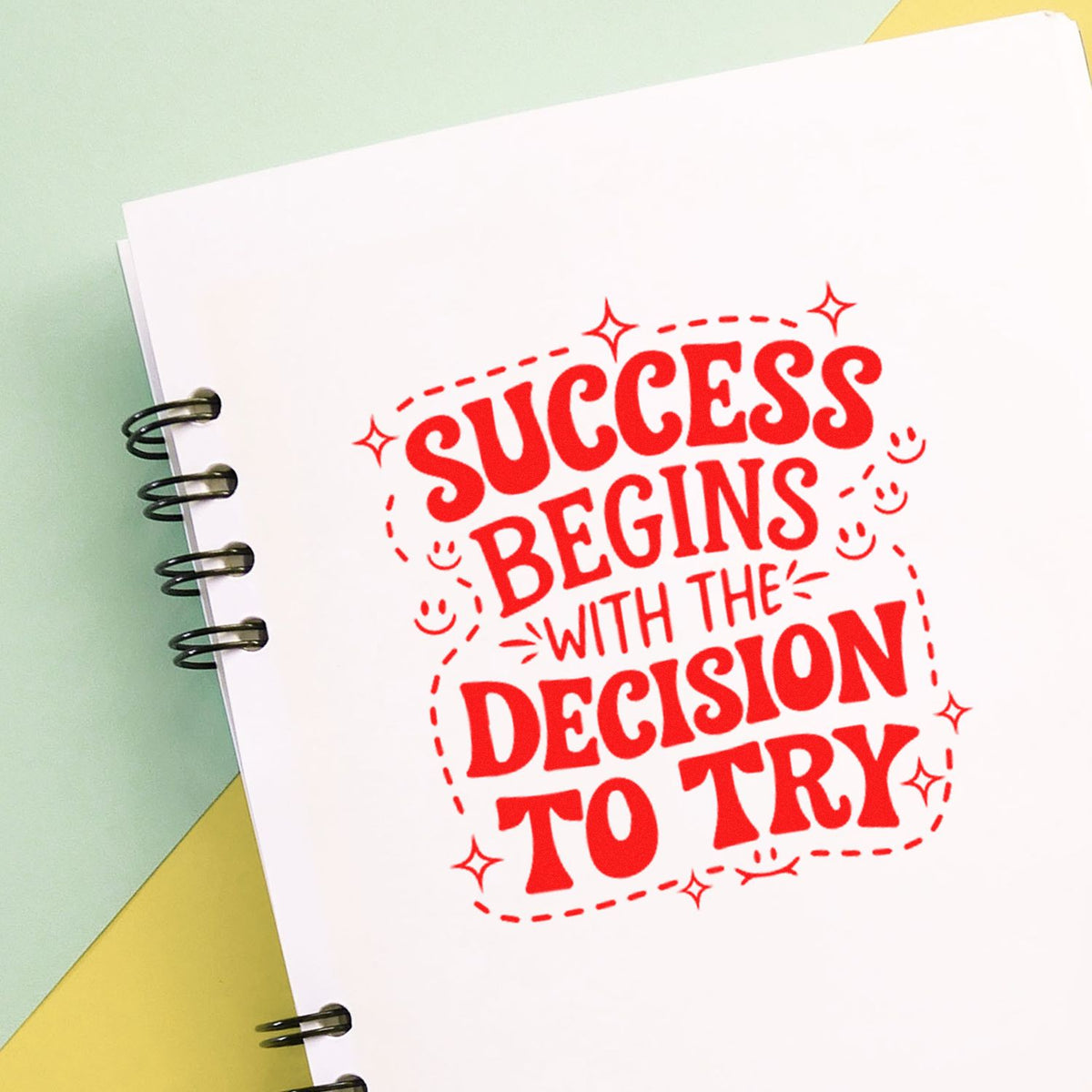 Red stamp seal on white spiral notebook page with Success Begins... over pastel green and yellow background.