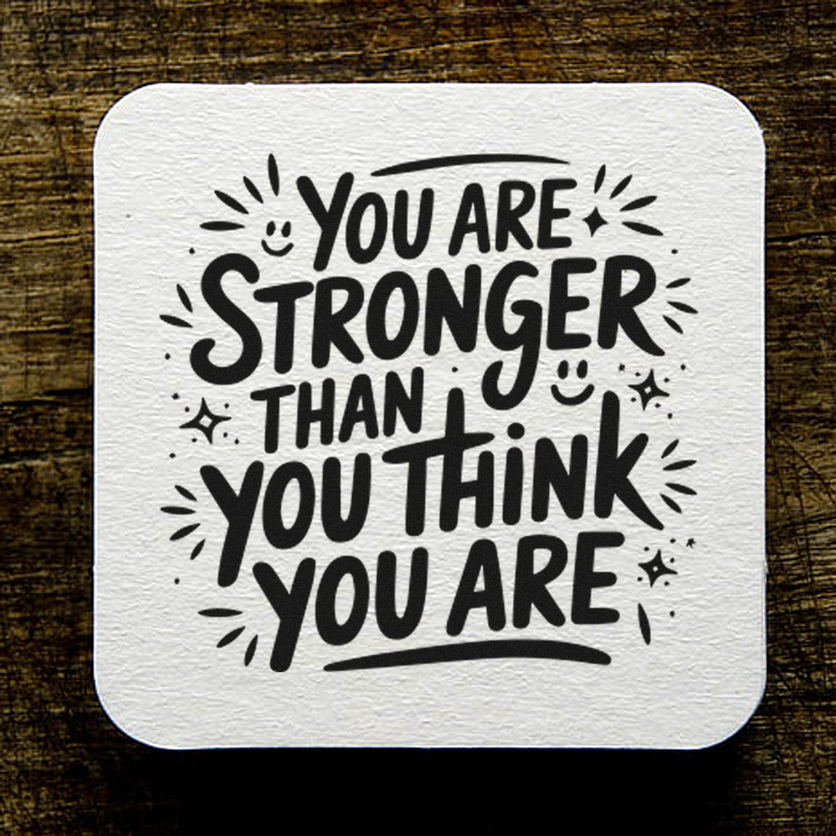 Square white textured seal stamp with bold black lettering, You are stronger than you think, on dark wood.