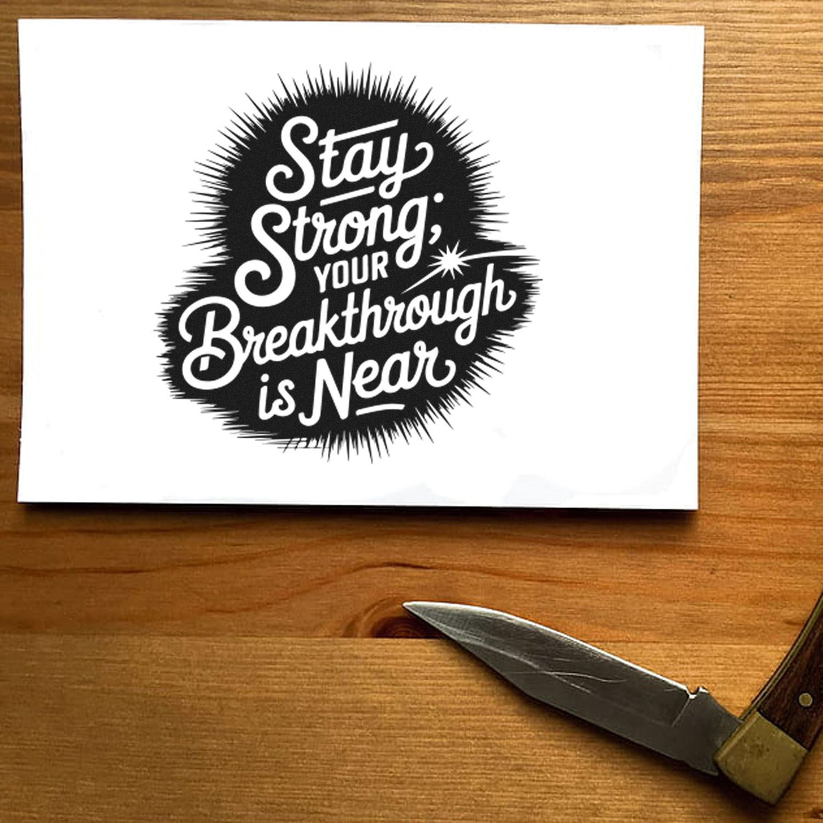 Black stamp seal with Stay Strong, your breakthrough is near on white paper over a wood table
