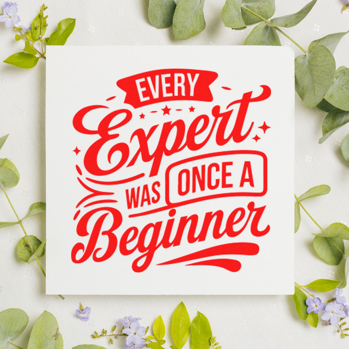 White stamp and seal with red retro lettering, Every Expert Was Once a Beginner, on a leafy floral background.