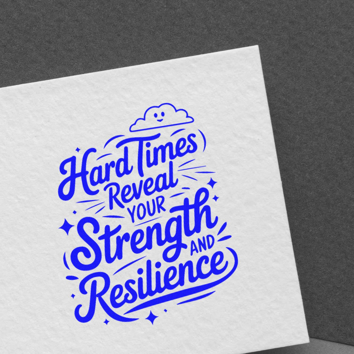 Blue rubber stamp seal on white paper reading Hard Times Revealed Your Strength and Resilience, with a smiling cloud and sparkles.